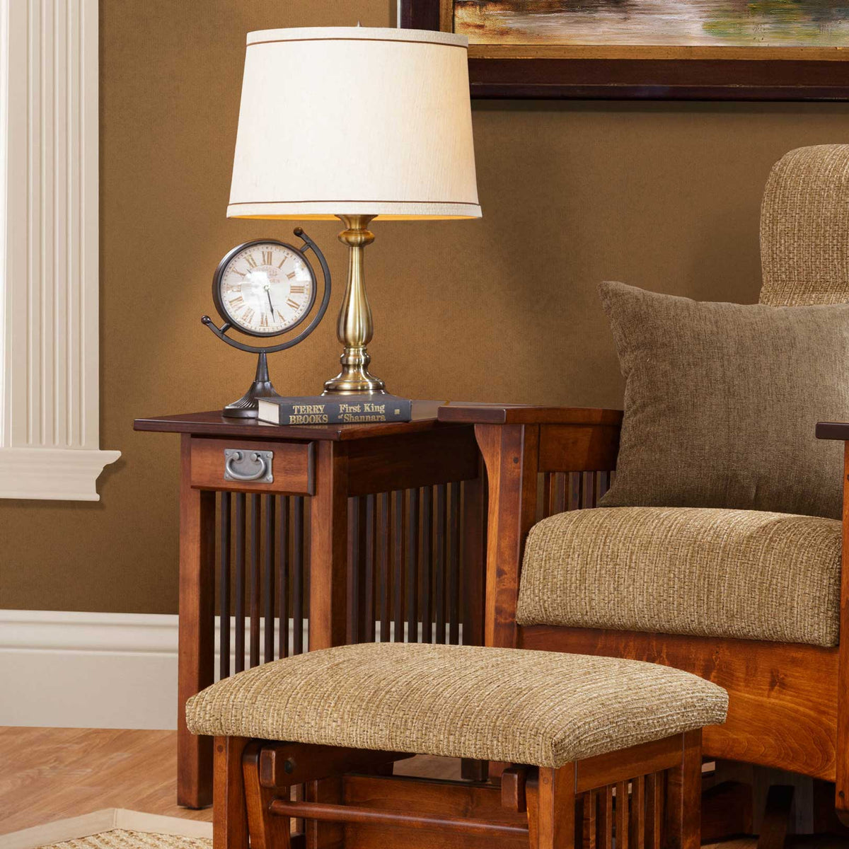 Dark cherry Mission end table with drawer and spindle sides holding a lamp, clock and books beside a glider ottoman