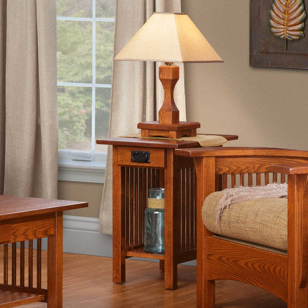 Oak Mission chairside end table with a drawer, black bail pull, spindle sides and lower shelf beside a slat arm chair