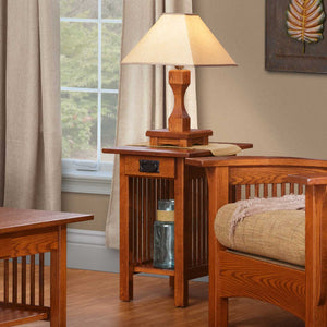 Oak Mission chairside end table with a drawer, black bail pull, spindle sides and lower shelf beside a slat arm chair