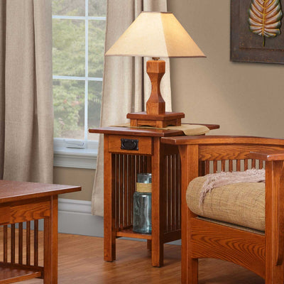Oak Mission chairside end table with a drawer, black bail pull, spindle sides and lower shelf beside a slat arm chair