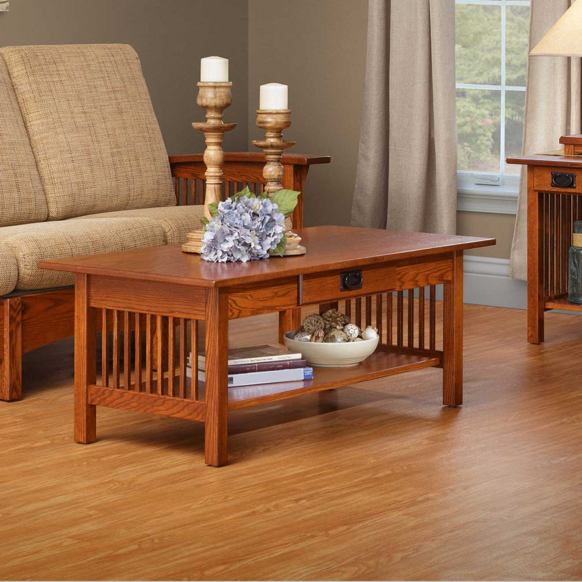Mission oak coffee table with drawer and lower shelf holding books and a bowl, styled with candlesticks and hydrangeas