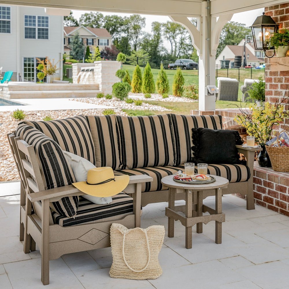 Weathered wood poly corner sectional sofa with black and tan striped cushions and a round side table under a pavilion