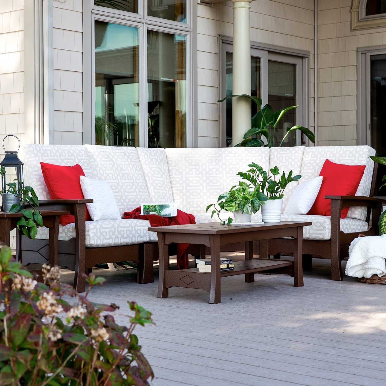 Brown poly corner sectional sofa with ivory patterned cushions, red accent pillows and a matching coffee table on a deck
