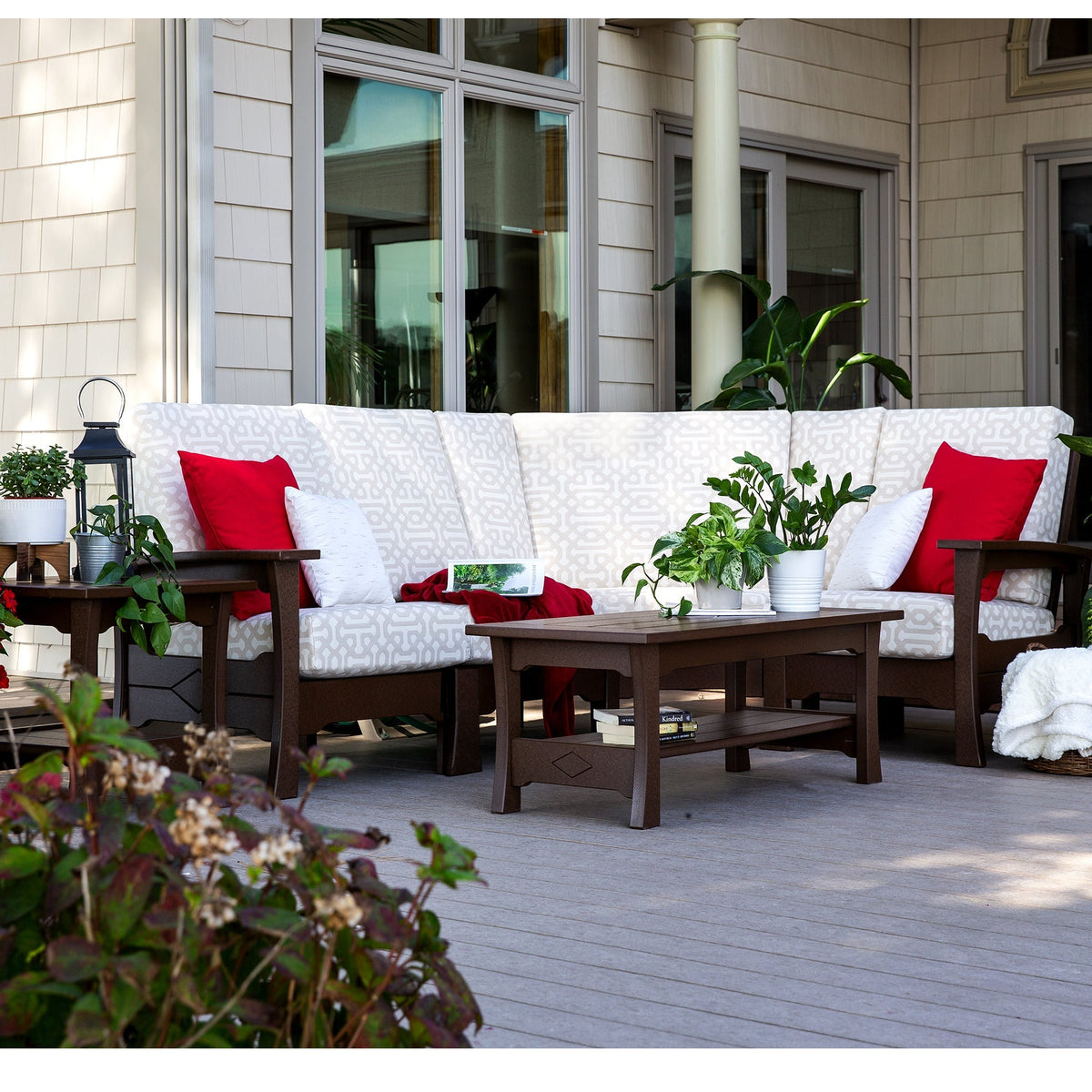 Brown poly patio sofa set with white patterned cushions, red pillows and a low coffee table with shelf on a deck