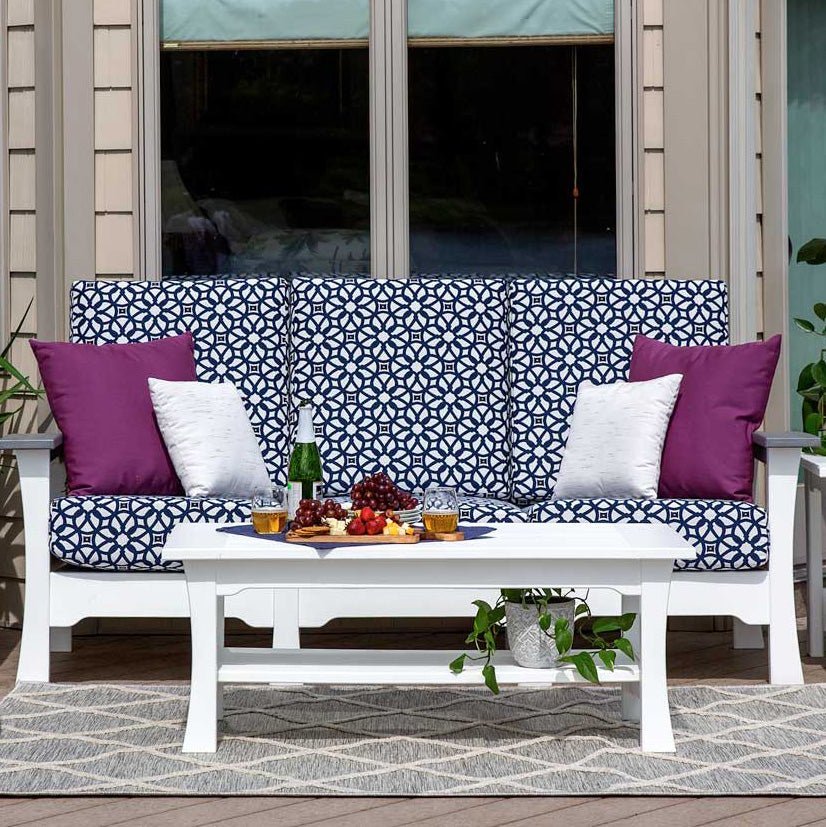 White poly patio sofa with navy and white geometric cushions, purple pillows and a white coffee table on a deck