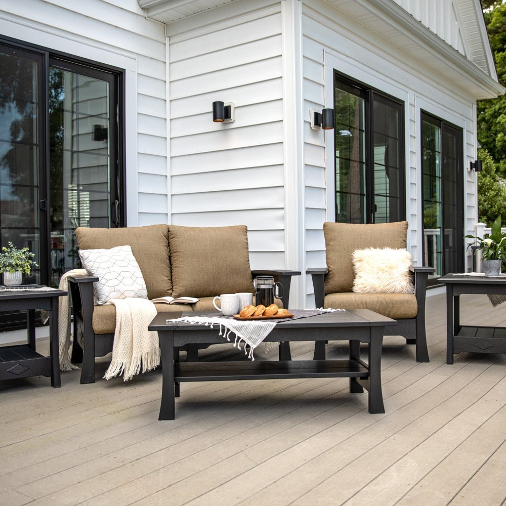 Black poly loveseat and chair with tan cushions and a slatted coffee table on a gray deck by white siding