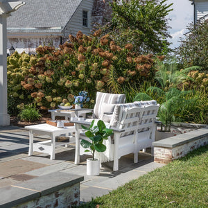 White poly loveseat set with gray striped cushions and two square end tables on a bluestone patio by hydrangeas