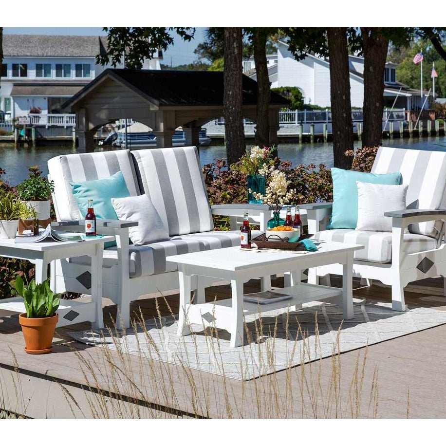 White poly loveseat and chair with gray striped cushions plus coffee and end tables on a waterfront deck