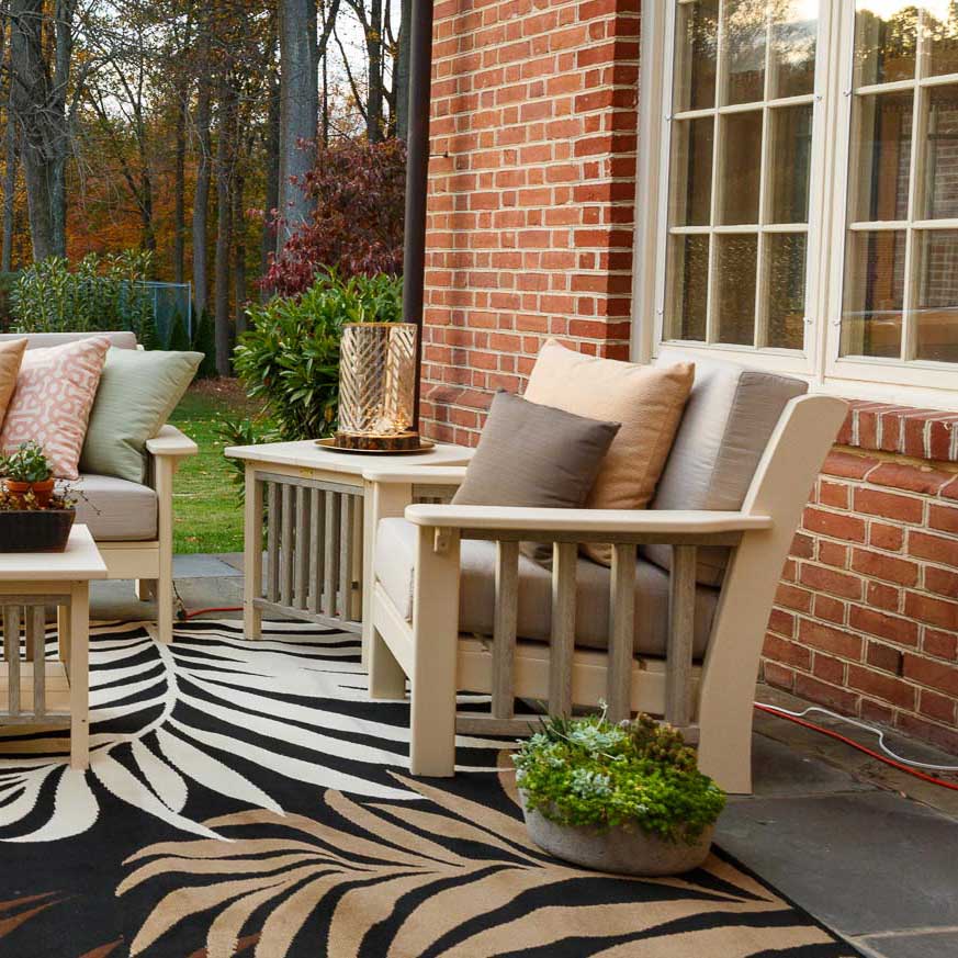Cream poly Mission cushion chairs and side tables with taupe pillows on a patterned rug by a brick house
