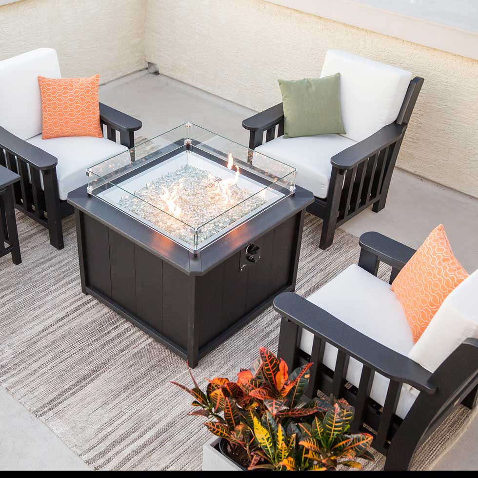 Four black poly Mission chairs with white cushions around a square gas fire pit table on a patio