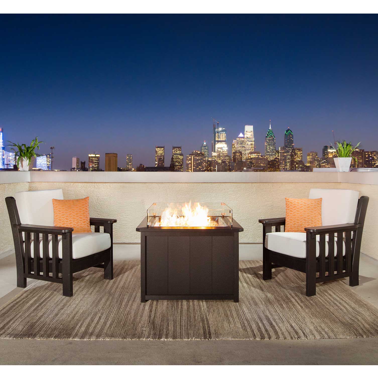 Two black poly Mission chairs with white cushions flanking a lit fire pit table on a city rooftop