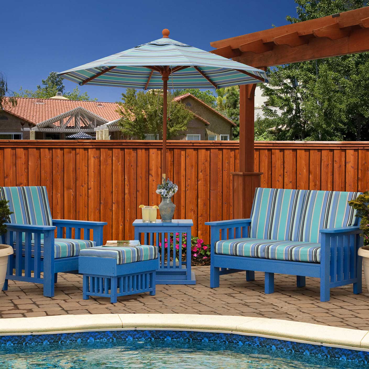 Blue poly Mission chairs, ottoman and side table with striped cushions under a striped umbrella by a pool