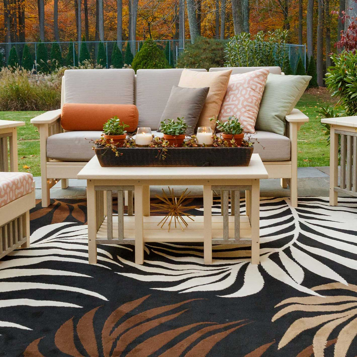 Cream poly Mission coffee table and cushioned sofa arranged on a black and tan patterned outdoor rug