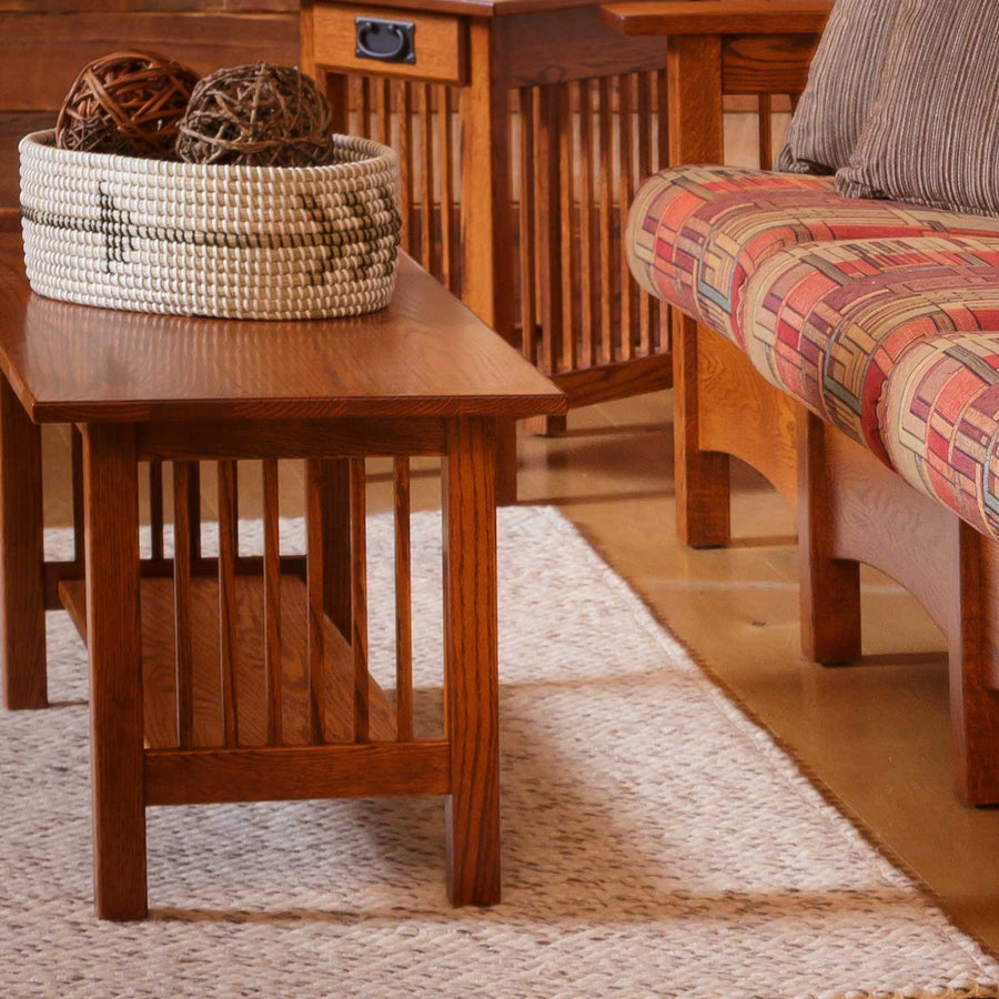 Small oak Mission coffee table with slat sides holding a woven basket, on a rug beside a patterned Mission loveseat