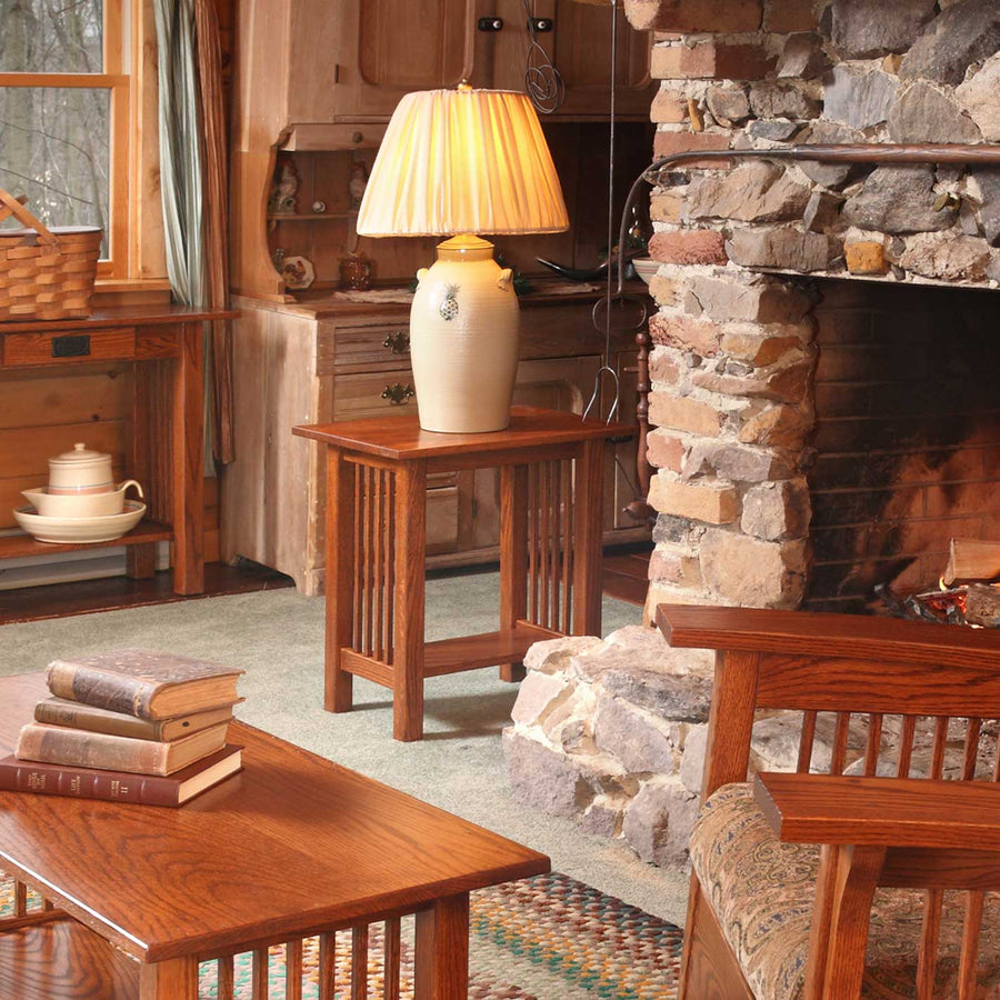 Oak Mission junior end table with slat sides holding a stoneware crock lamp beside a stone fireplace