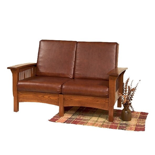 Brown leather Mission Morris loveseat in oak with spindle side panels, shown on a white background with a plaid rug