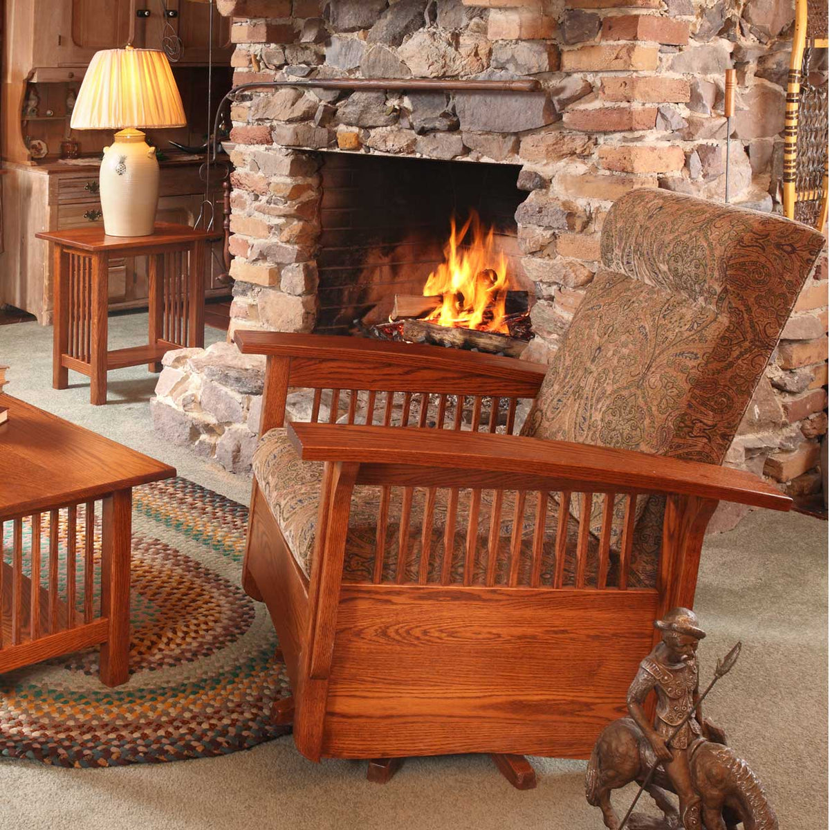 Side view of an oak swivel glider with paisley cushions and slat panel arms facing a stone hearth fire