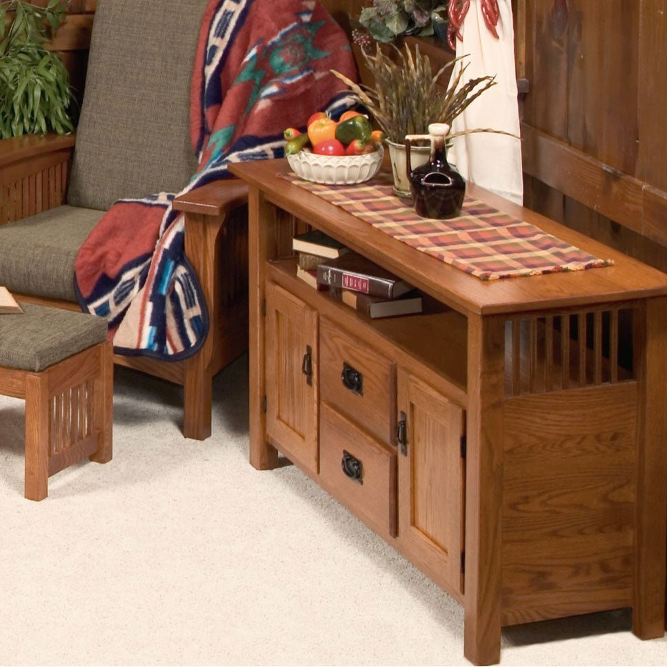 Oak Mission tv cabinet with drawers and doors styled with a plaid runner, fruit bowl and crock beside a Mission chair