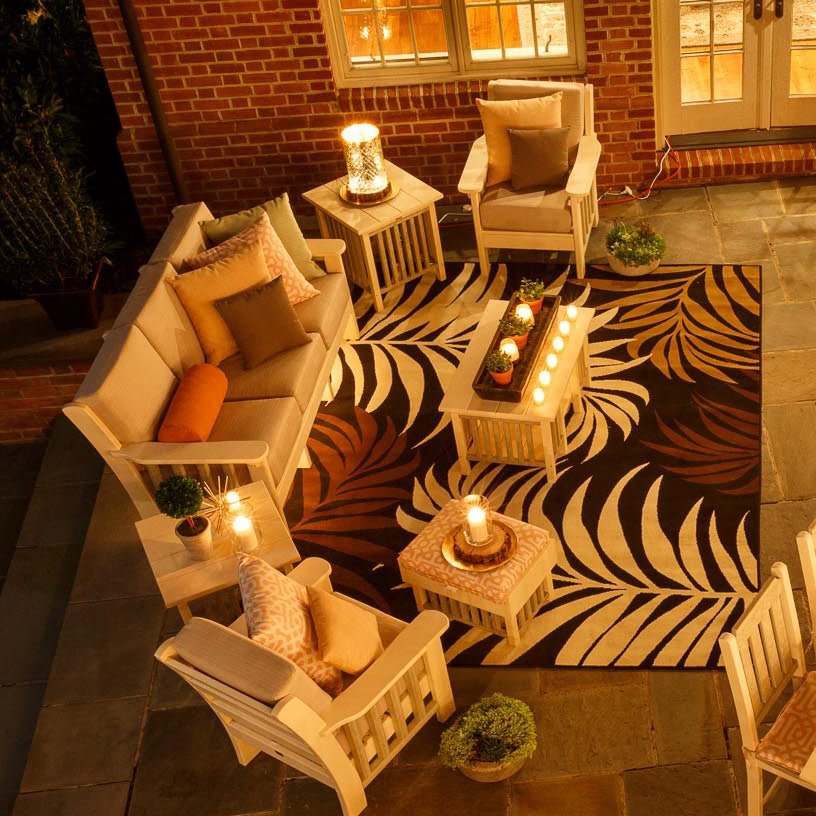 Overhead night view of a cream poly Mission patio sofa set with candles on a patterned outdoor rug
