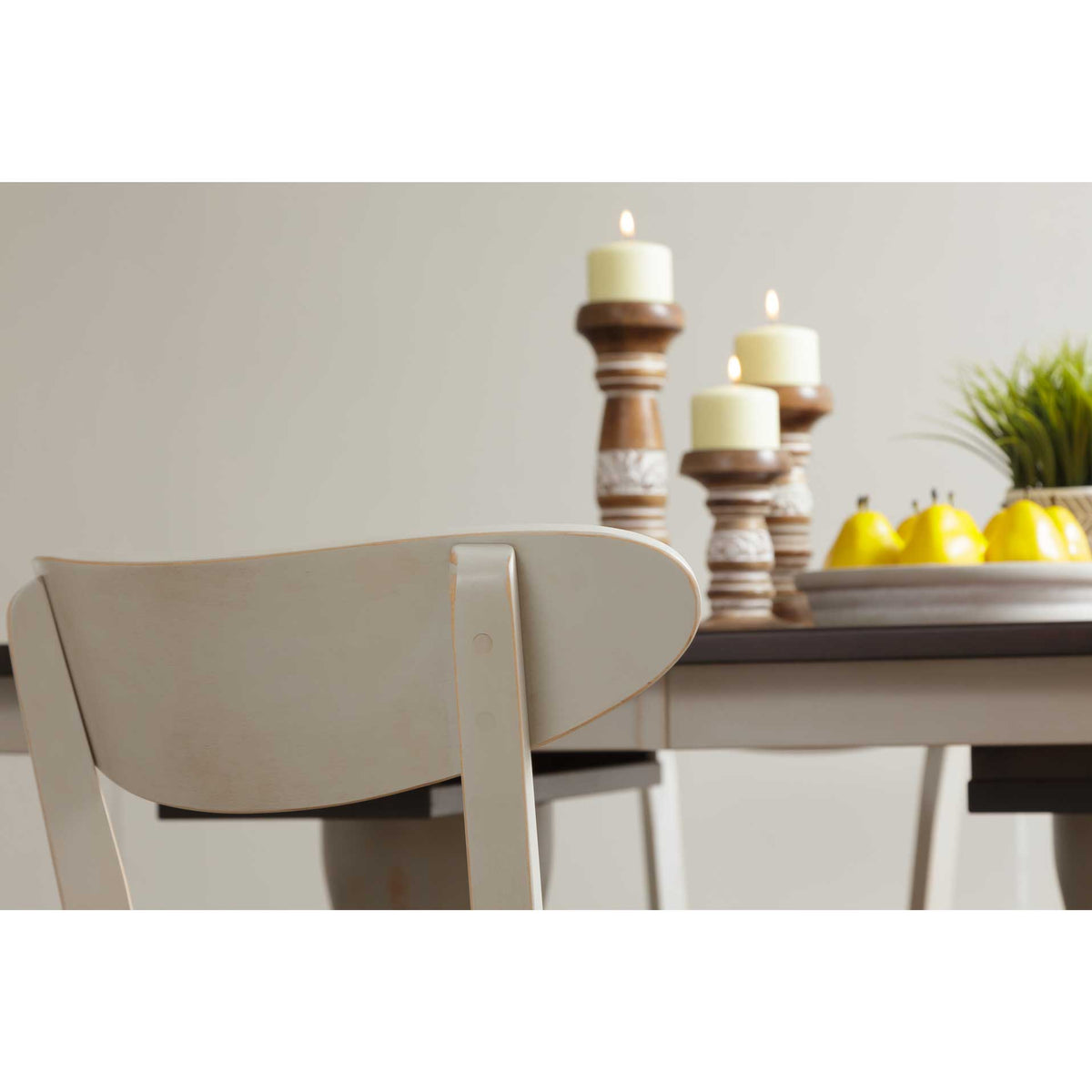 Close-up of a cream painted chair back with a curved crest rail beside candles and lemons on the table