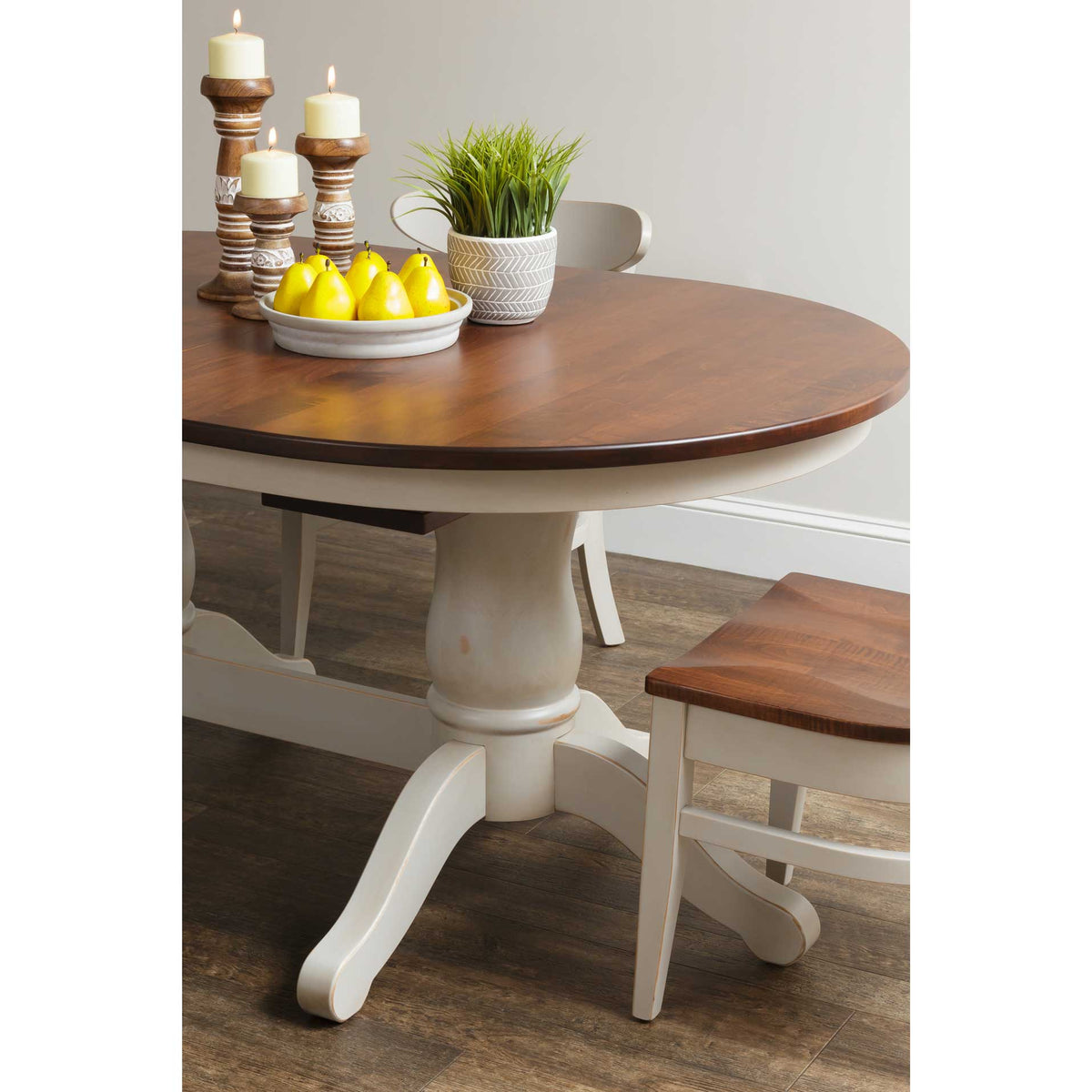 Round-end view of the two-tone dining table with a turned cream pedestal, styled with pears and candles