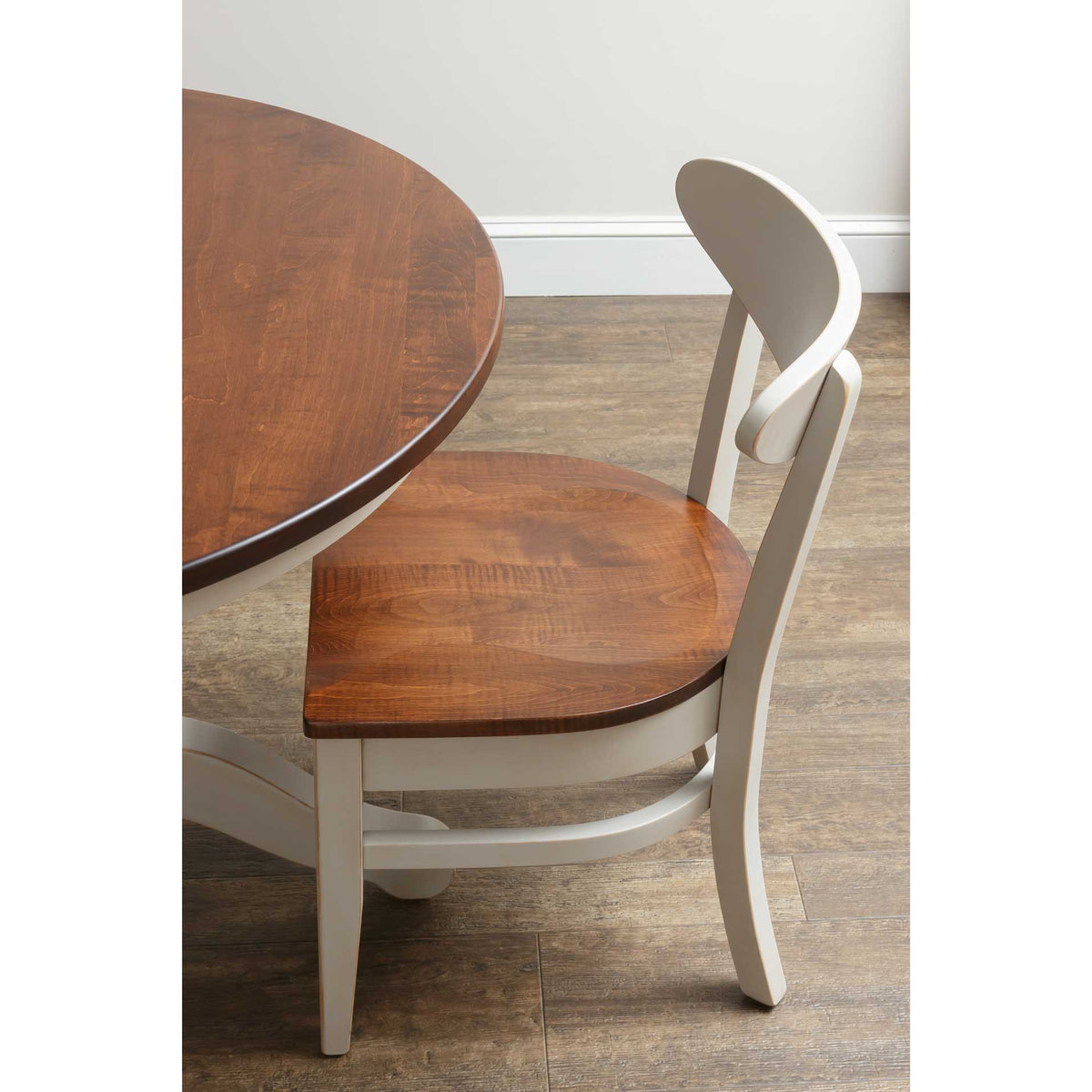 Cream painted dining chair with a curved back and stained wood seat viewed beside a round table