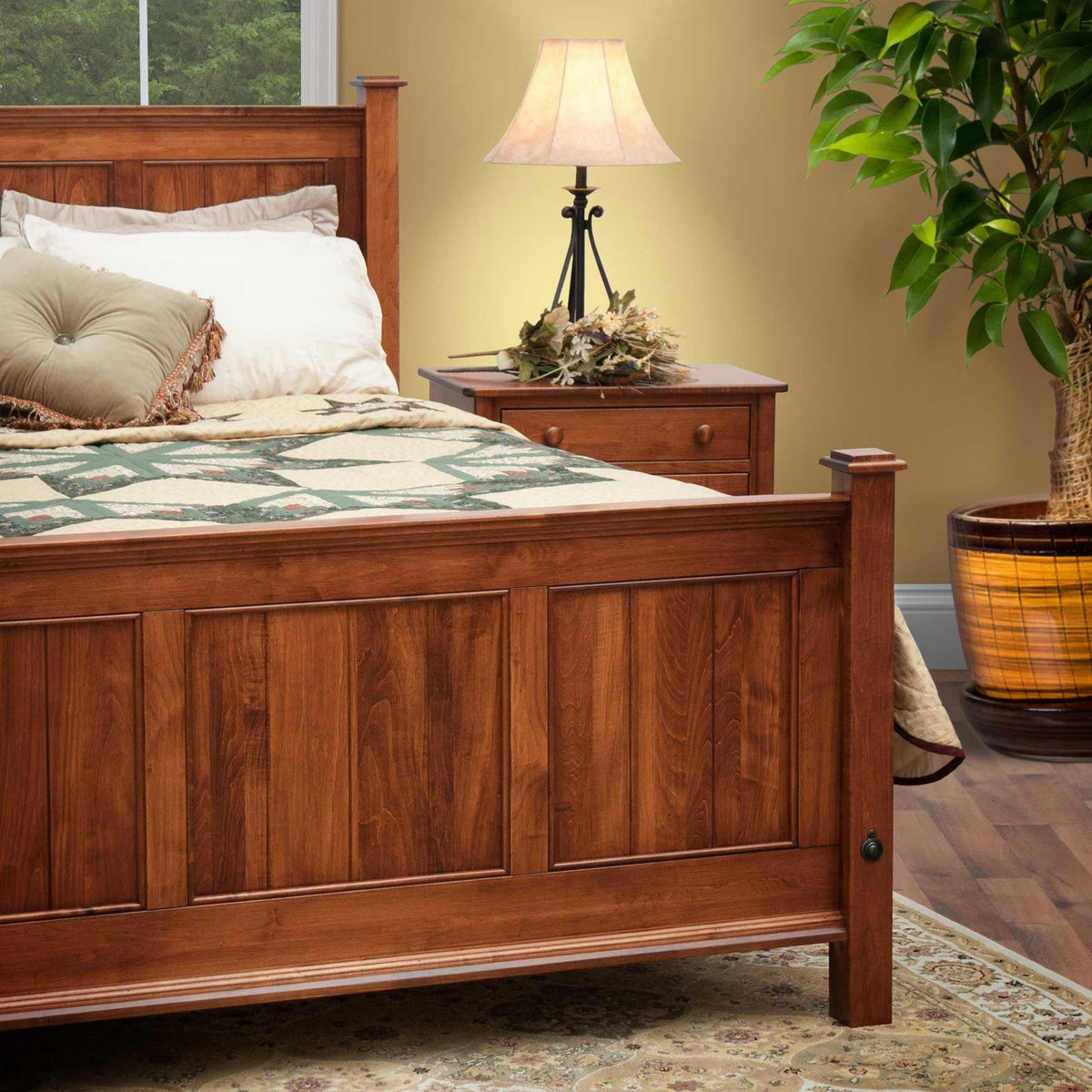 Close-up of a cherry panel bed footboard and nightstand with lamp, dried flowers and a green star quilt