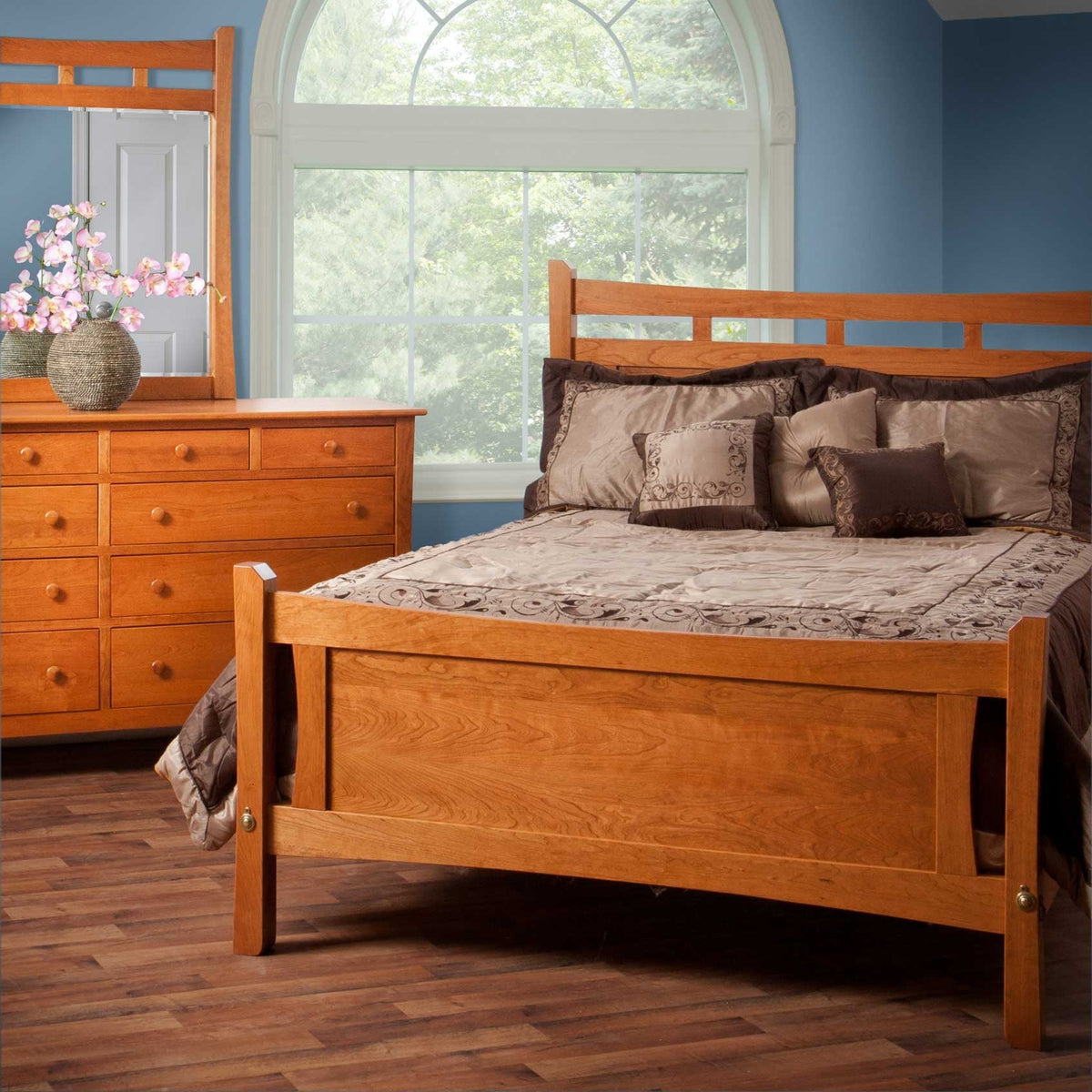 Cherry panel bed footboard and dresser with mirror in a blue bedroom with an arched window