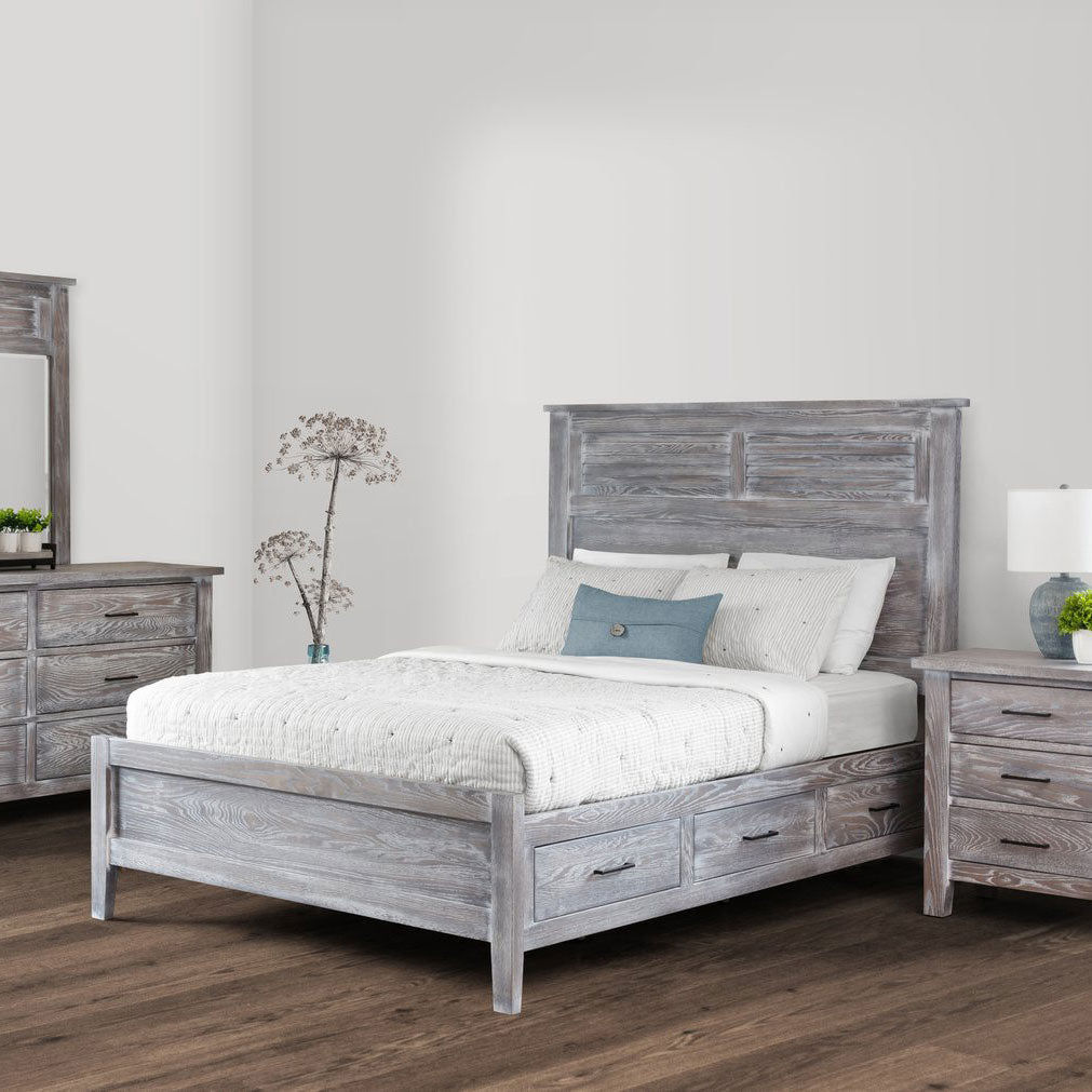 Weathered gray louver panel storage bed with three footboard drawers in a bright bedroom with dresser