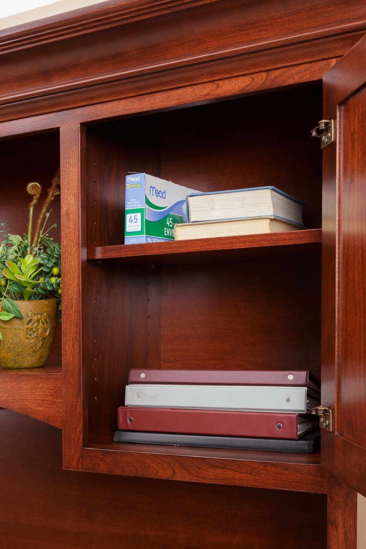 Hutch cabinet with its raised panel door open, showing an adjustable shelf holding binders and envelopes
