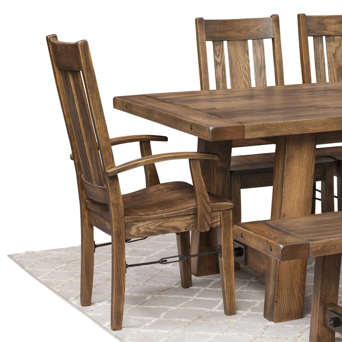 Honey brown oak dining arm chair with slat back and iron rod stretcher beside a trestle table and bench