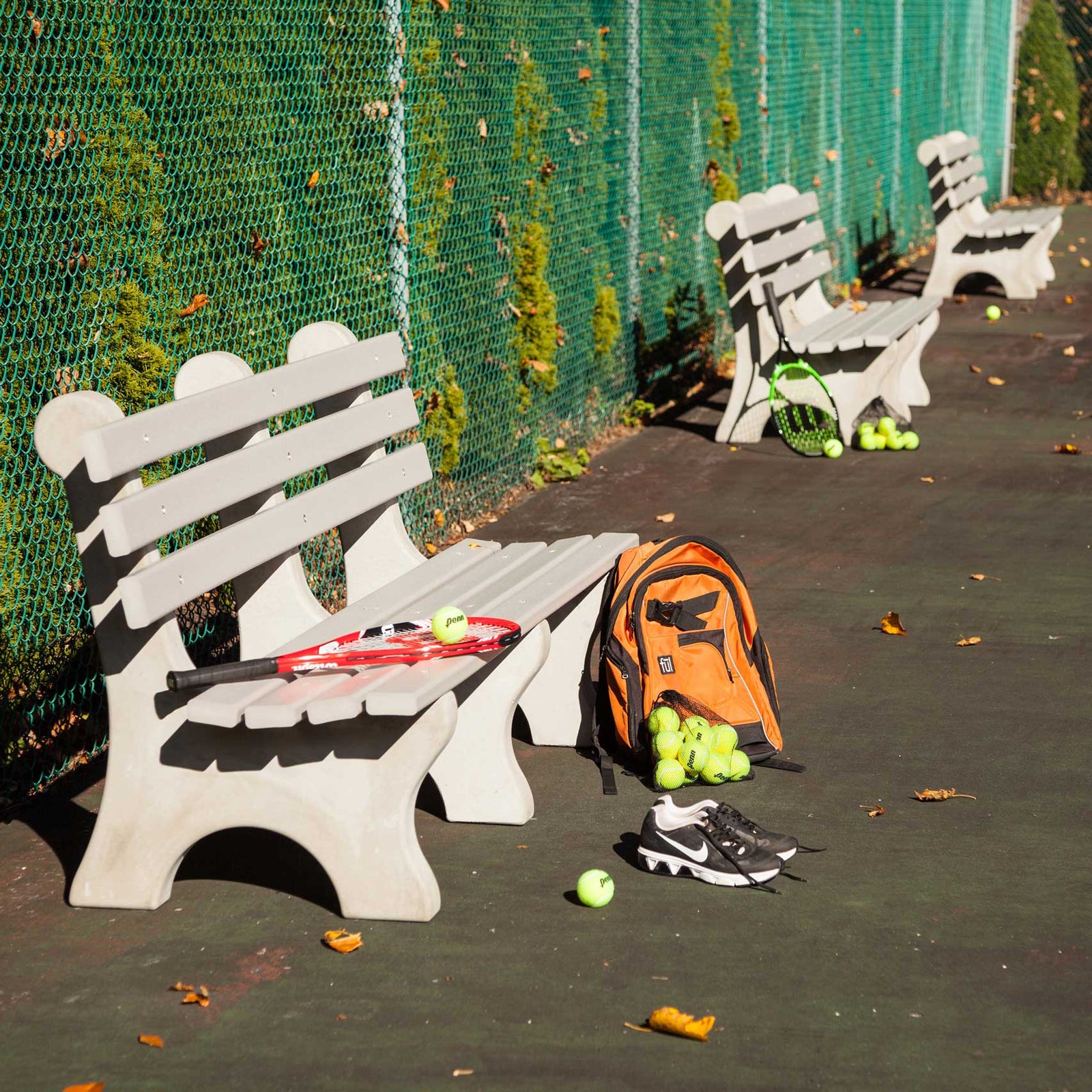 Brown poly lumber park bench with three back slats and curved legs, styled with a blue throw and books on fallen leaves