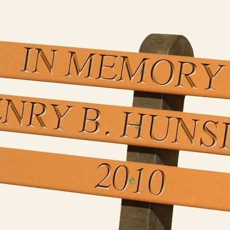 Close up of engraved memorial lettering routed into the cedar poly back slats of a park bench, reading in memory and 2010