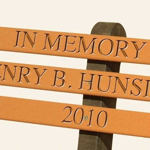 Close up of engraved memorial lettering routed into the cedar poly back slats of a park bench, reading in memory and 2010