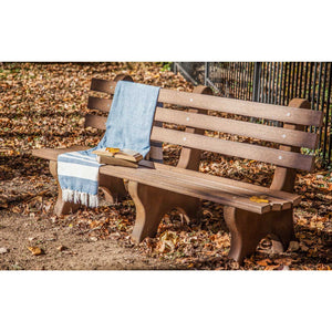 Brown poly lumber park bench with three back slats and curved legs, styled with a blue throw and books on fallen leaves