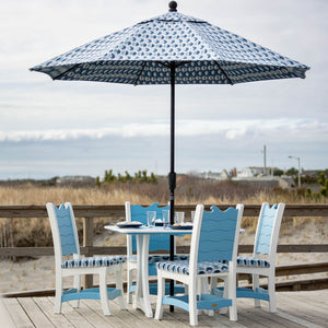 White and blue wave poly dining set for four under a patterned market umbrella on a boardwalk overlooking dunes