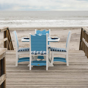 Square wave back poly dining table and four chairs with blue tie dye cushions on a beach boardwalk facing the surf
