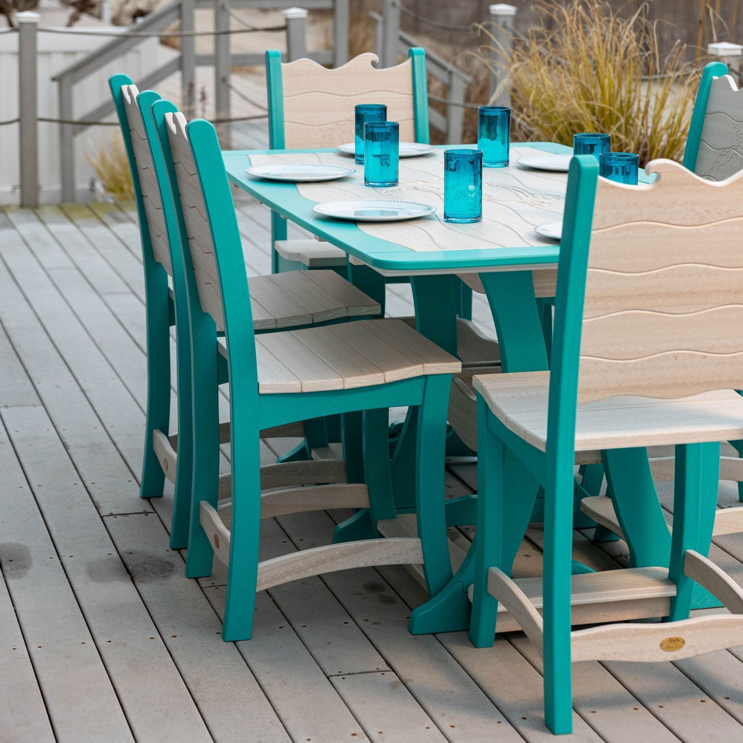 Aruba blue and driftwood poly counter dining table with six wave back chairs set with plates and blue glasses on a deck