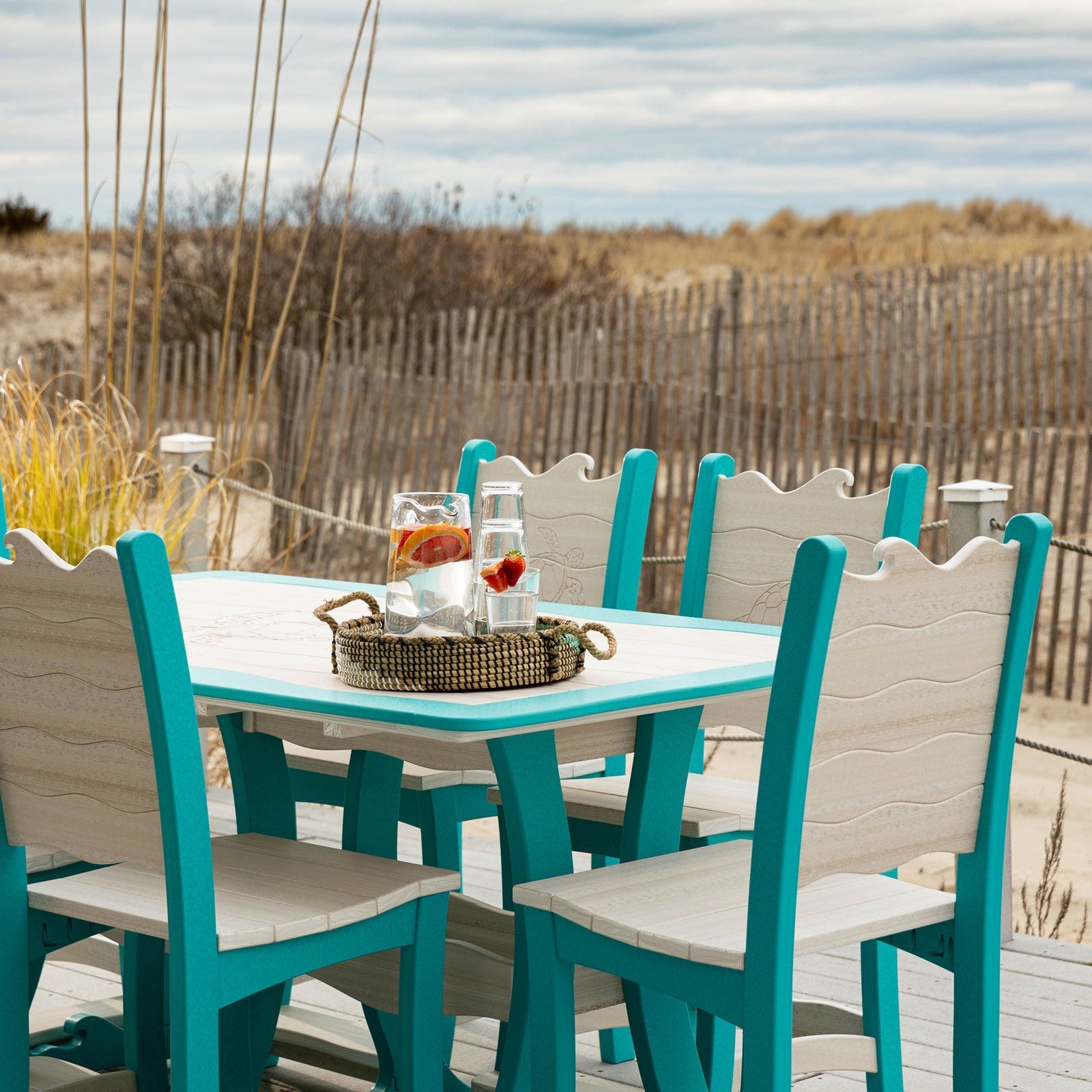 Aruba blue and driftwood poly counter dining table with six wave back chairs set with plates and blue glasses on a deck