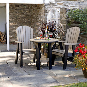 Weatherwood and black poly 30 inch round patio pub table with two tall fan back Adirondack chairs on a stone patio