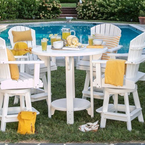 White poly round bar height table with four swivel Adirondack chairs and yellow pillows on grass beside a pool