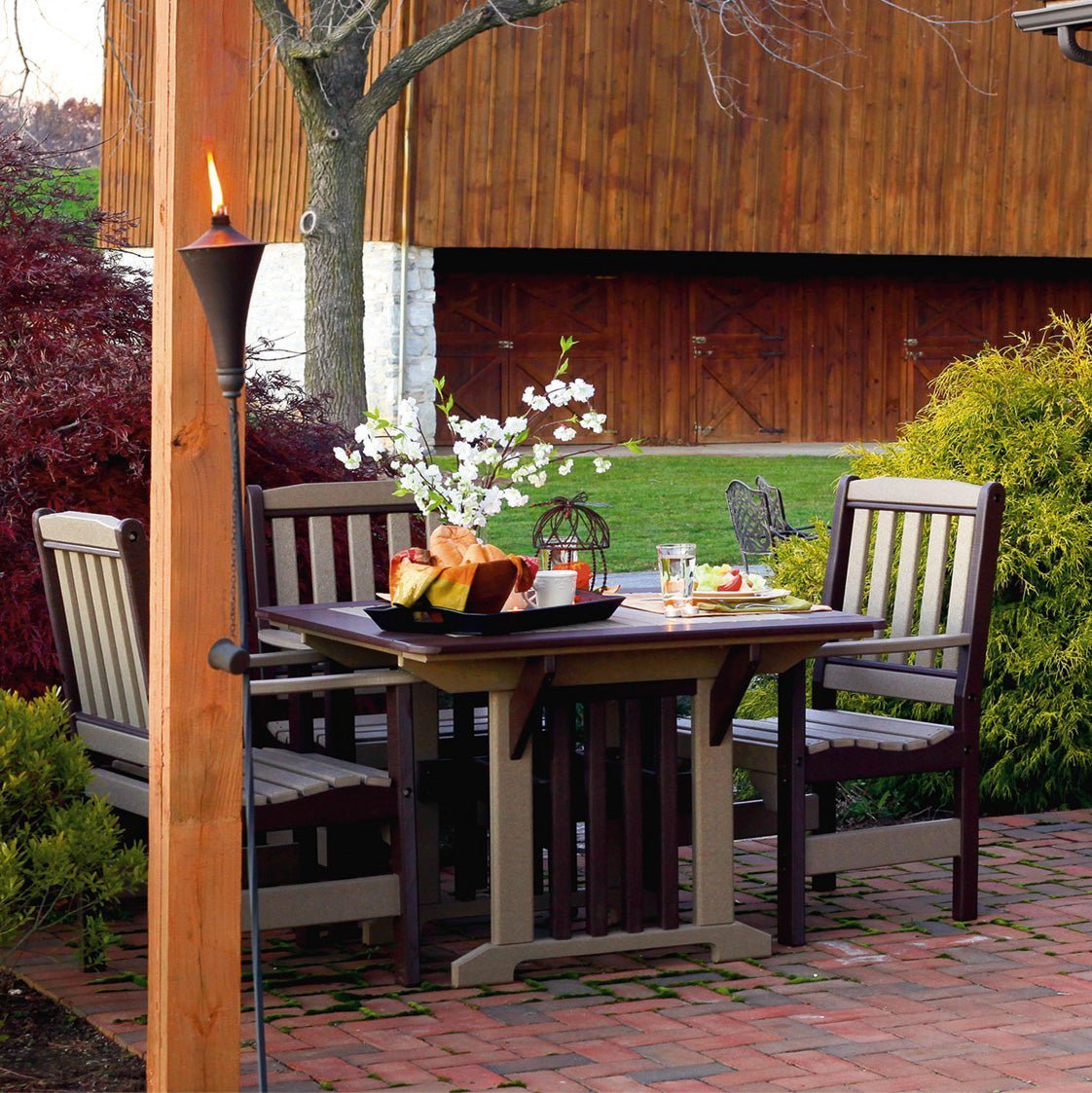 Black and gray poly English Garden patio dining table with four slat back arm chairs set for dinner under a pergola