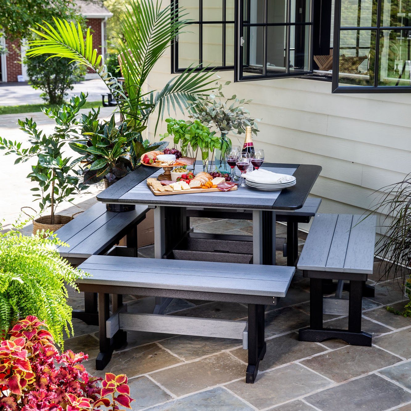 Gray and black poly English Garden patio dining table with two matching backless benches set with wine and cheese