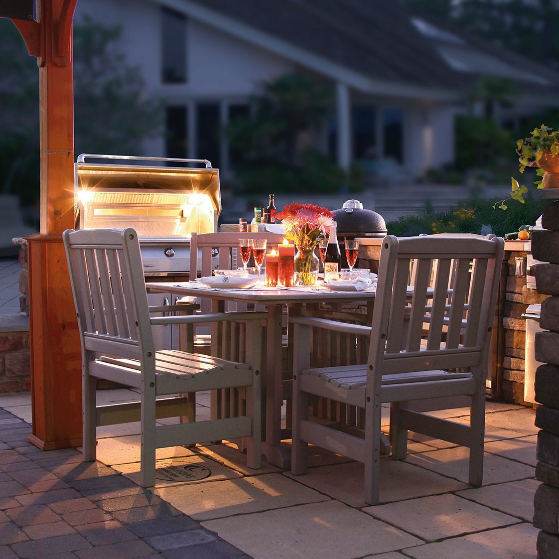 Driftwood gray poly English Garden patio dining table and four slat back chairs beside a lit outdoor grill at night