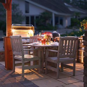 Driftwood gray poly English Garden patio dining table and four slat back chairs beside a lit outdoor grill at night