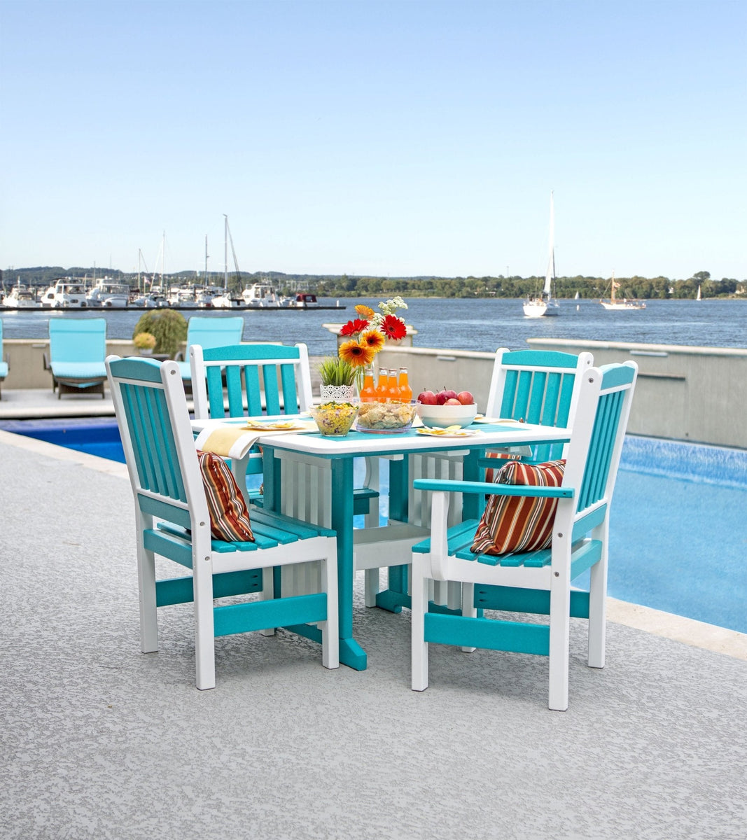 Aruba blue and white poly English Garden patio dining table with four slat back arm chairs by a marina pool