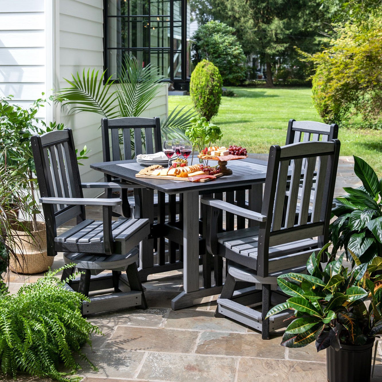 Slate gray poly English Garden square patio table with four swivel arm chairs set with charcuterie on a flagstone patio