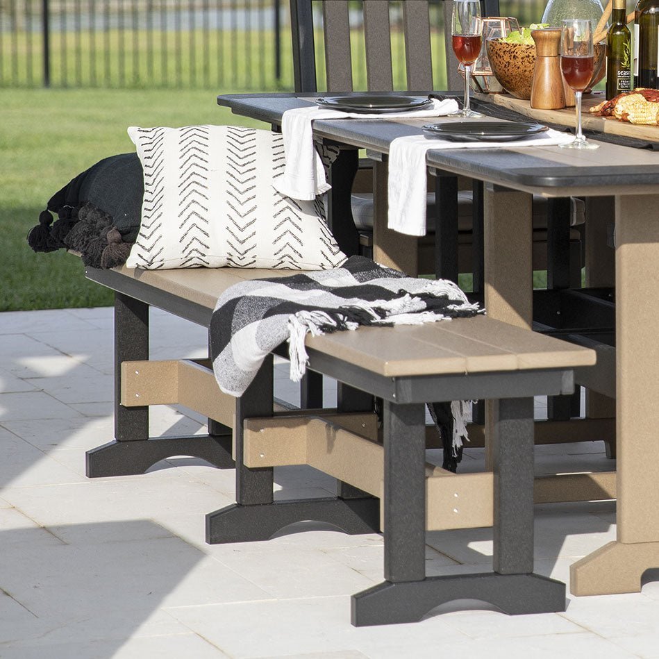 Pair of weatherwood and black poly backless patio benches with pillows and throws pulled up to a patio dining table