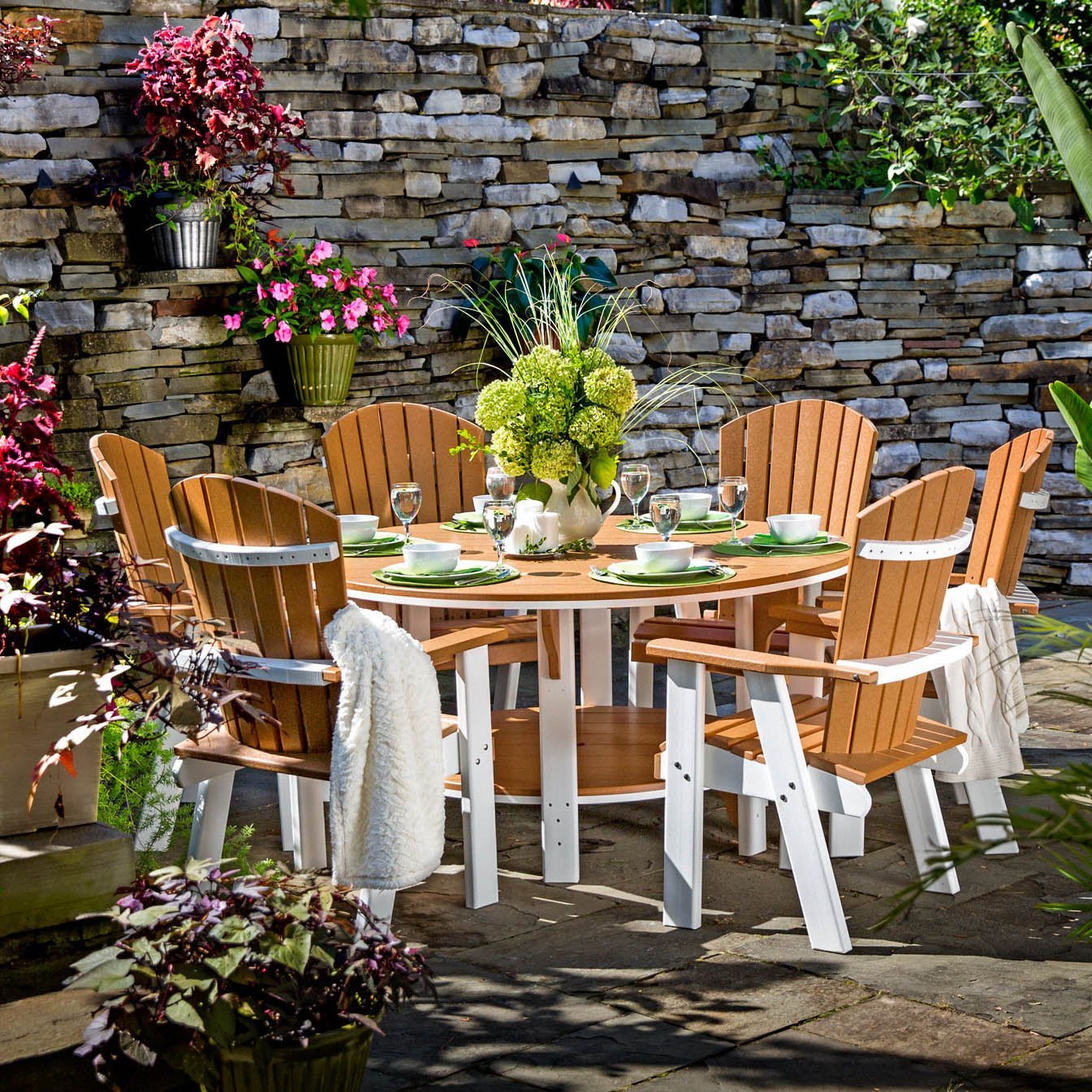Cedar and white poly 60 inch round bistro dining table with six fan back chairs on a patio by a stone wall