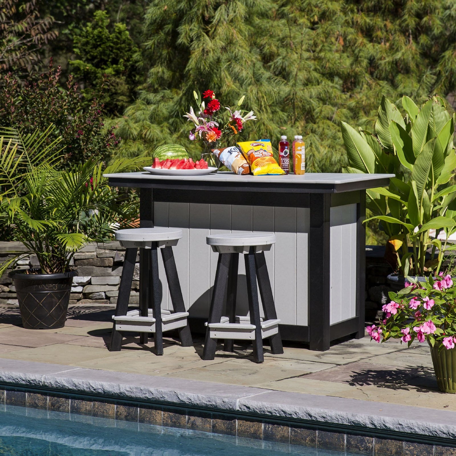 Black and light gray poly outdoor bar island with two swivel backless stools set with snacks beside a pool